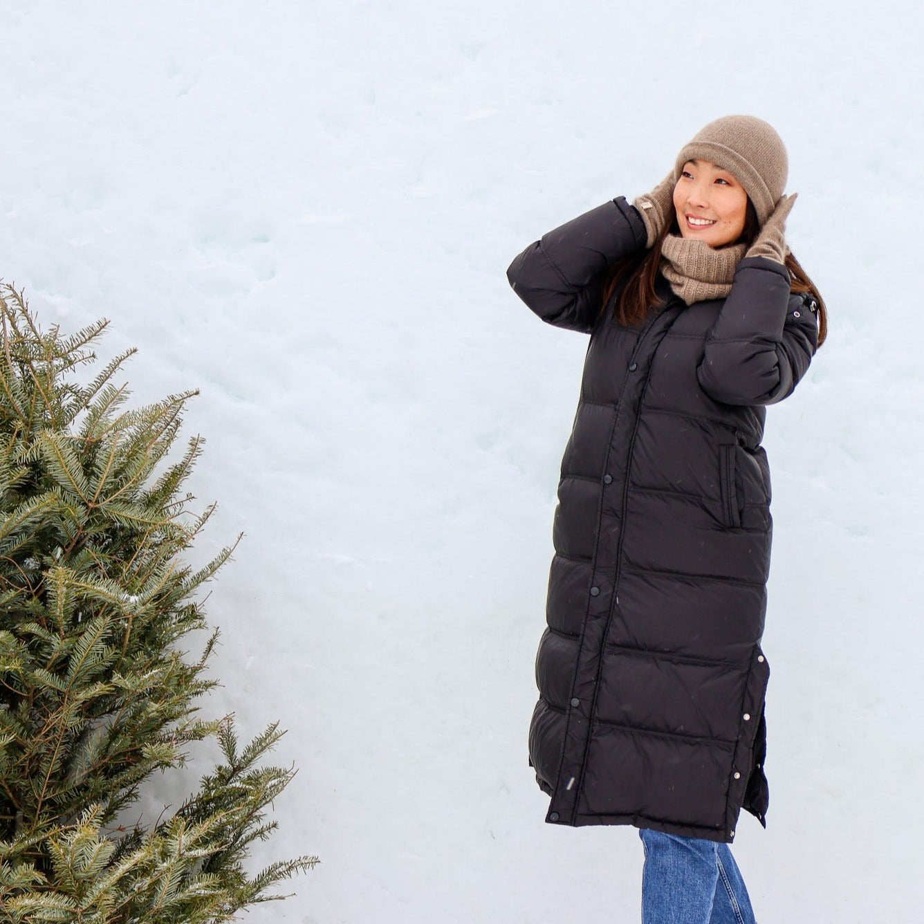 A woman wearing a Cashmere Infiniti Scarf outside surrounded by snow and an evergreen tree